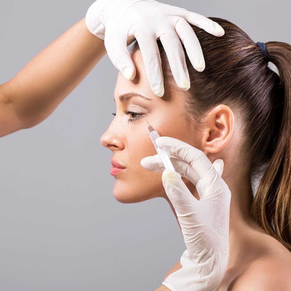 A woman receiving a facial injection from a gloved professional.