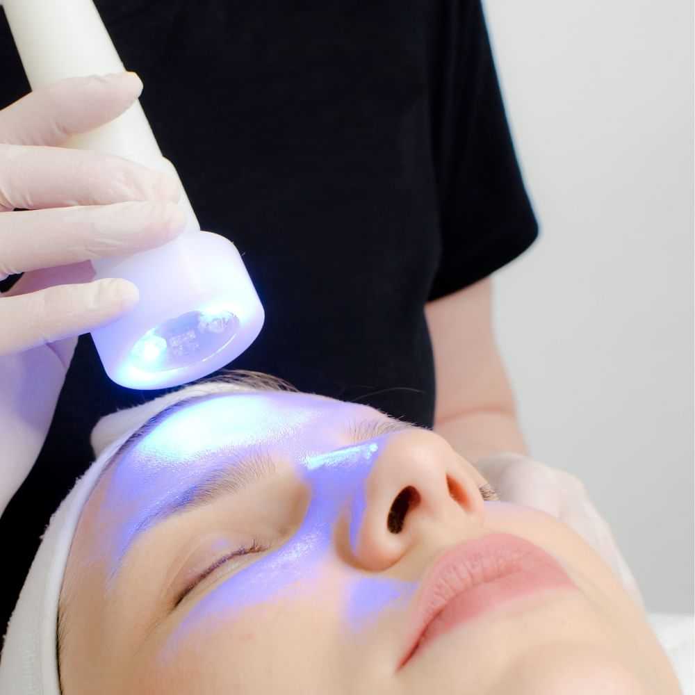 Person receiving facial skin treatment with light therapy device.