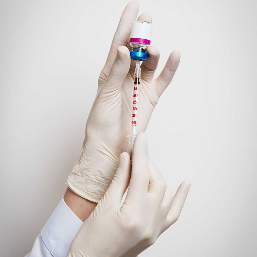 Person in gloves filling a syringe with vaccine from vial.