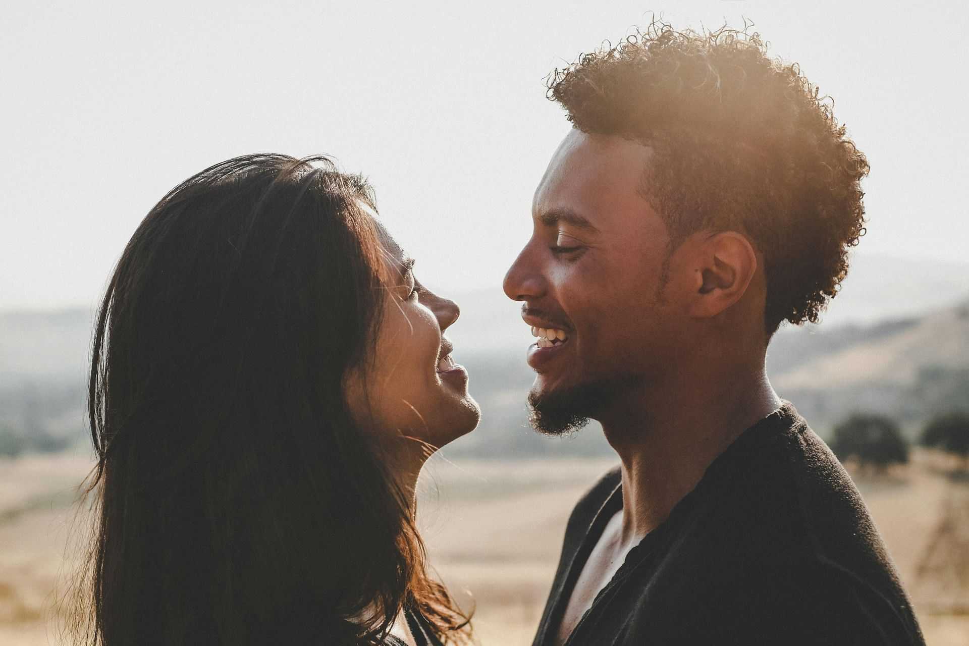 Two people smiling at each other in a sunny field.